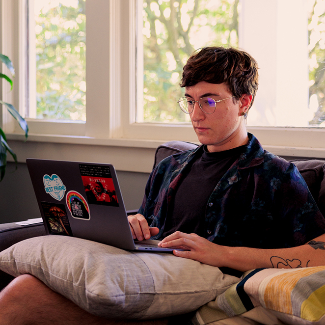 DJ Drakos sitting on a couch, staring intently at something on their laptop